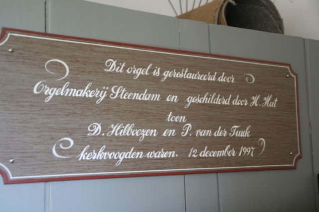 Gedenkbord orgel; 'Dit orgel is gerestaureerd door Orgelmakerij en geschilderd door H. Hut toen D. Hilboezen en P. van der Tuuk kerkvoogden waren. 12 december 1997'